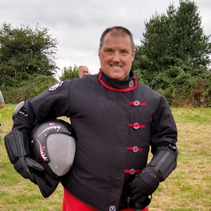 Commercial Officer Shaun in field wearing black fencing jacket and holding fencing face guard under arm