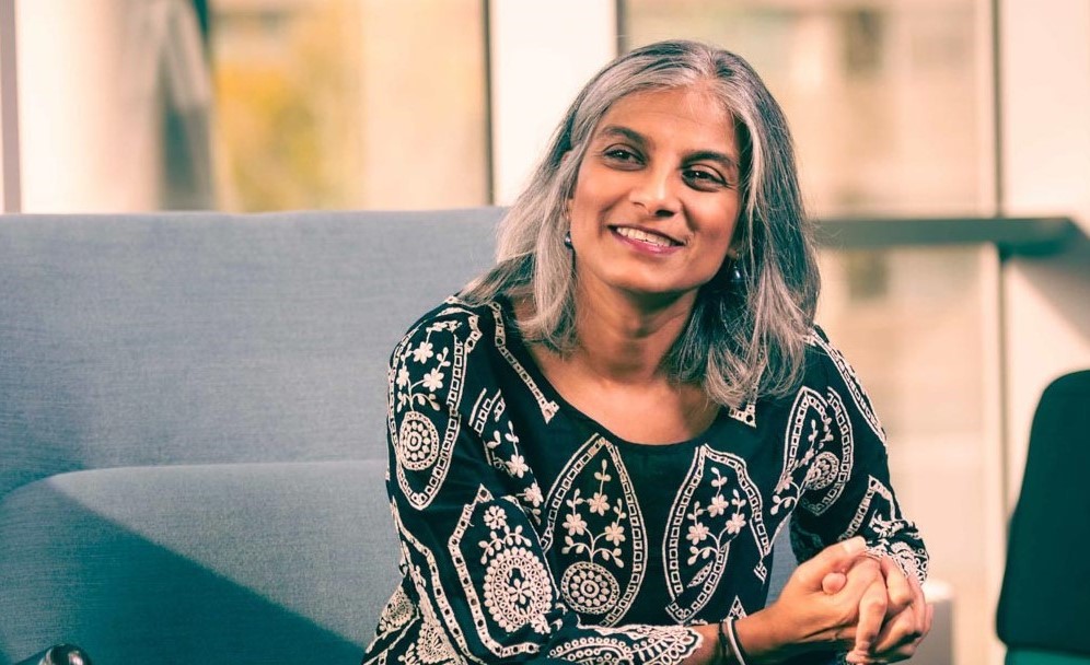 Woman sitting on a sofa with grey hair in black and white print pattern blouse .