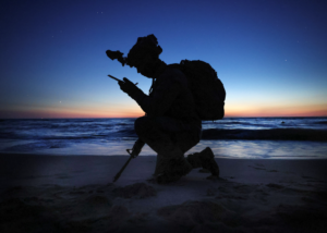 A soldier in silhouette uses a radio on a beach