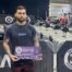 Liam Smith holding an award with row of cross trainers behind him